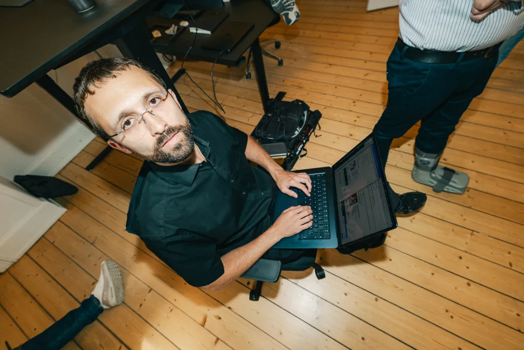 Medarbejder med bærbar computer i skødet ser op fra arbejdet midt i kontoret