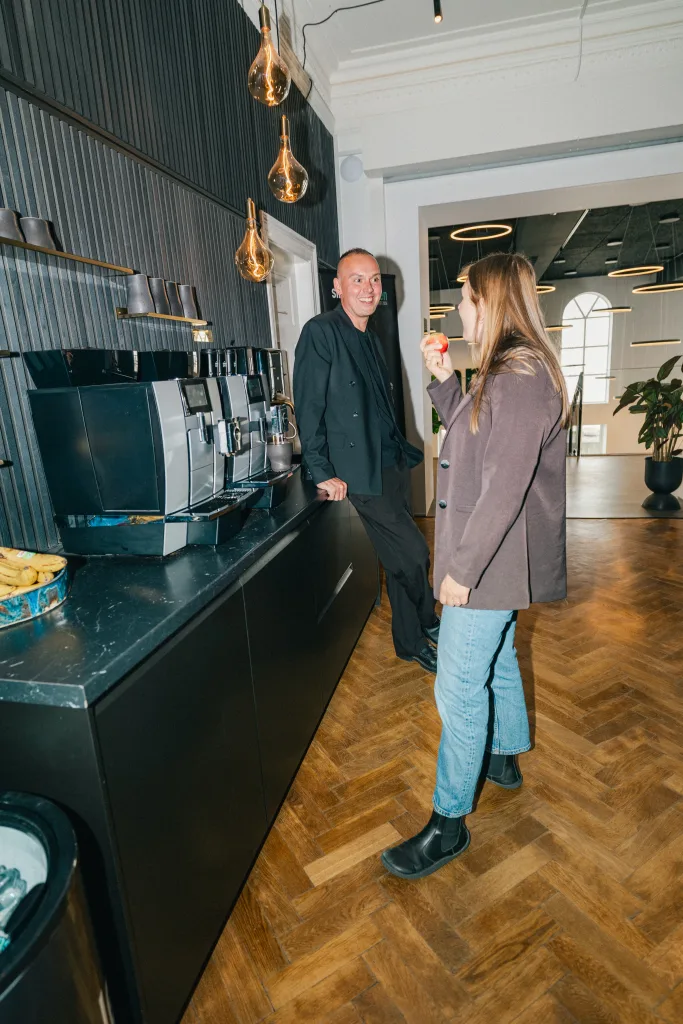 To kolleger taler sammen ved kaffemaskinerne, hvor månedens marketing bliver vendt