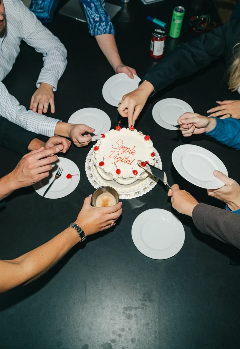 Kolleger samlet om en lagkage med teksten Simple Digital set fra oven