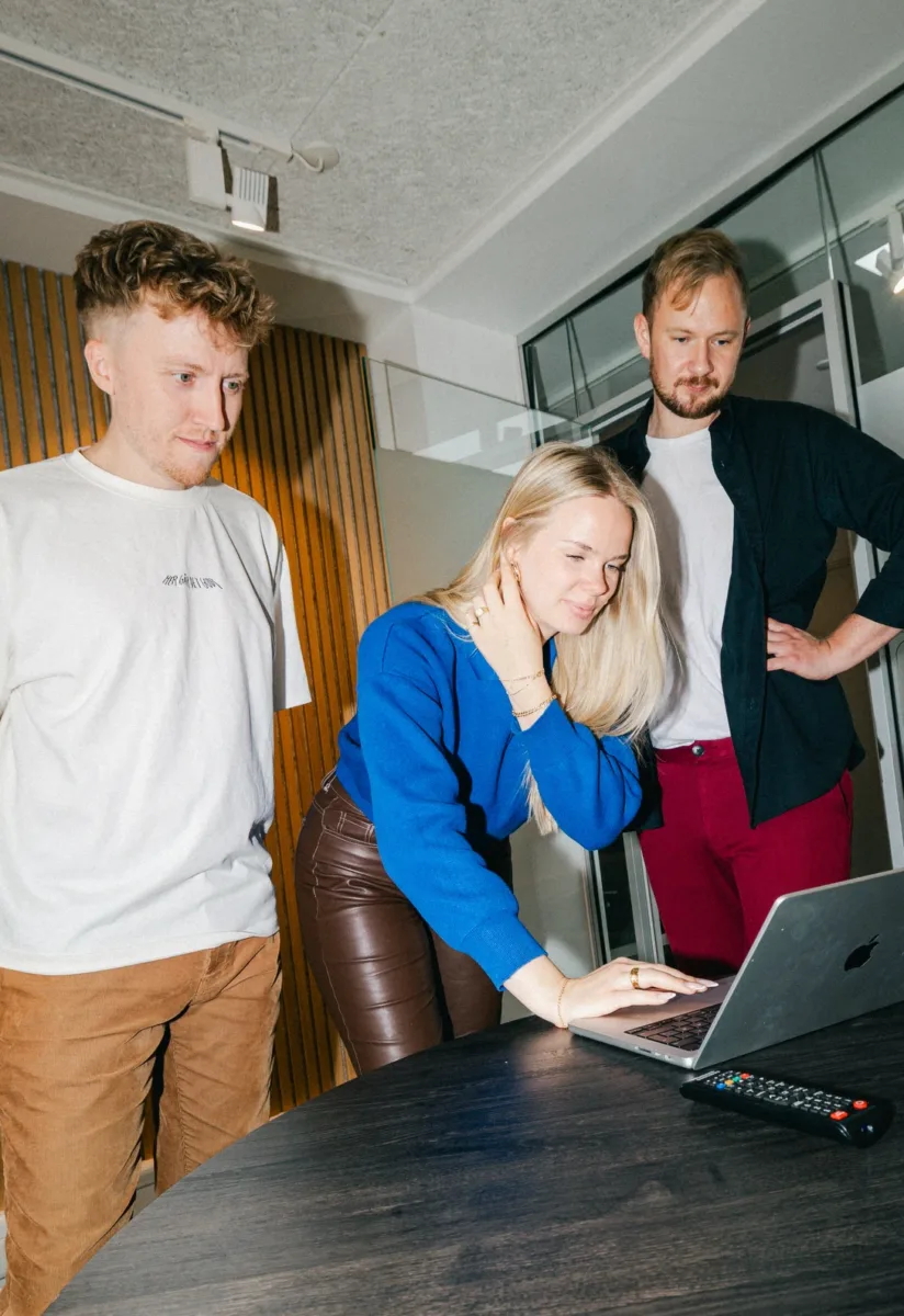 Tre kolleger ser på en bærbar computer i mødelokalet med glasvæg og følger leads