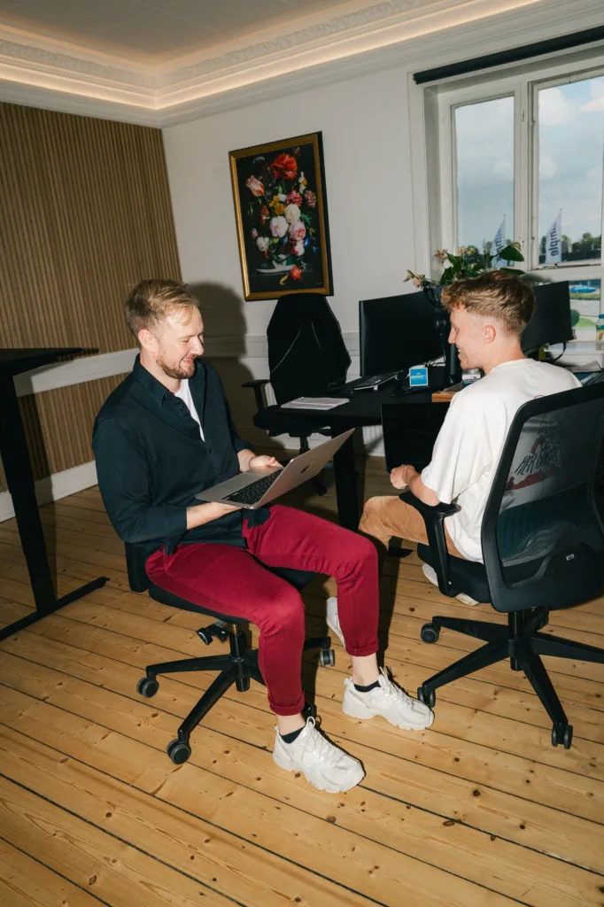 To kolleger vender sig mod hinanden i kontorstolene og gennemgår Google Shopping tallene